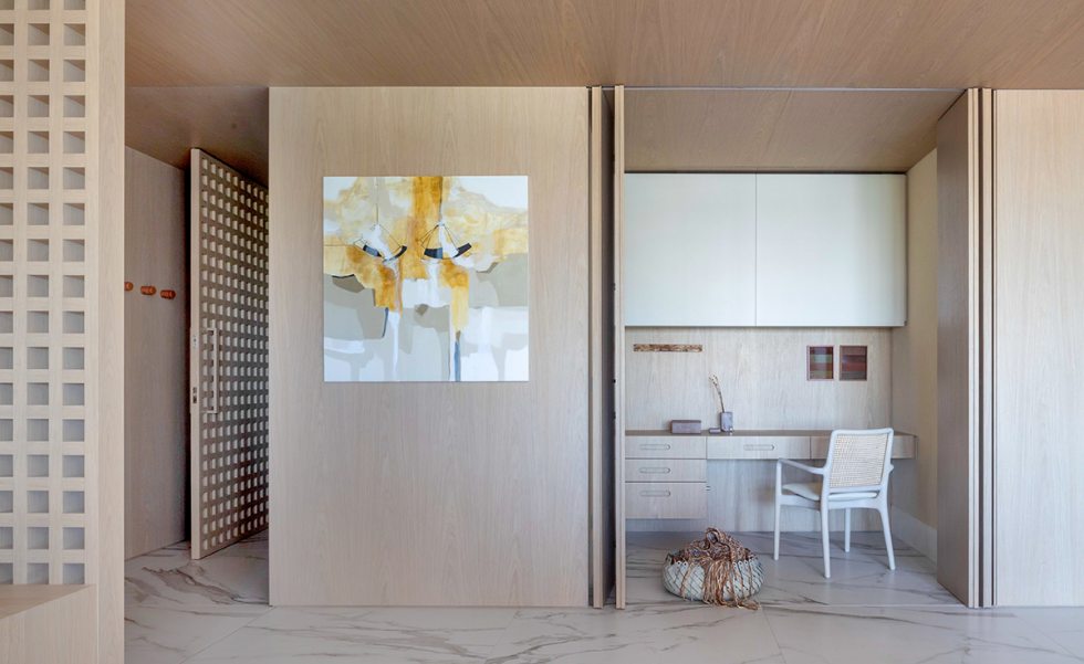 O hall de entrada comporta um pequeno home office que pode ser separado do restante do espaço através das portas retráteis. A madeira natural Rovere aparece em toda a marcenaria O hall de entrada comporta um pequeno home office que pode ser separado do restante do espaço através das portas retráteis. A madeira natural Rovere aparece em toda a marcenaria