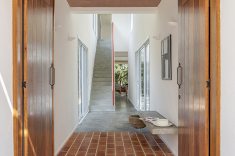 Piso de tijolo cerâmico e porta de madeira marcam a entrada da casa.