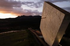 - A arquitetura se destaca na paisagem de Brumadinho, com o volume iluminado em contraste com as montanhas ao fundo.