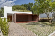 A casa foi construída em terreno com declive nos fundos.  A entrada, no térreo, com volume branco simples contrasta com o bloco terracota da garagem, que introduz a paleta de cores do projeto.