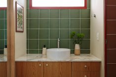 O banheiro da suíte mantém a intensidade das cores vermelho na esquadria e verde intenso nos azulejos. A bancada tem cuba de apoio Celite Slim